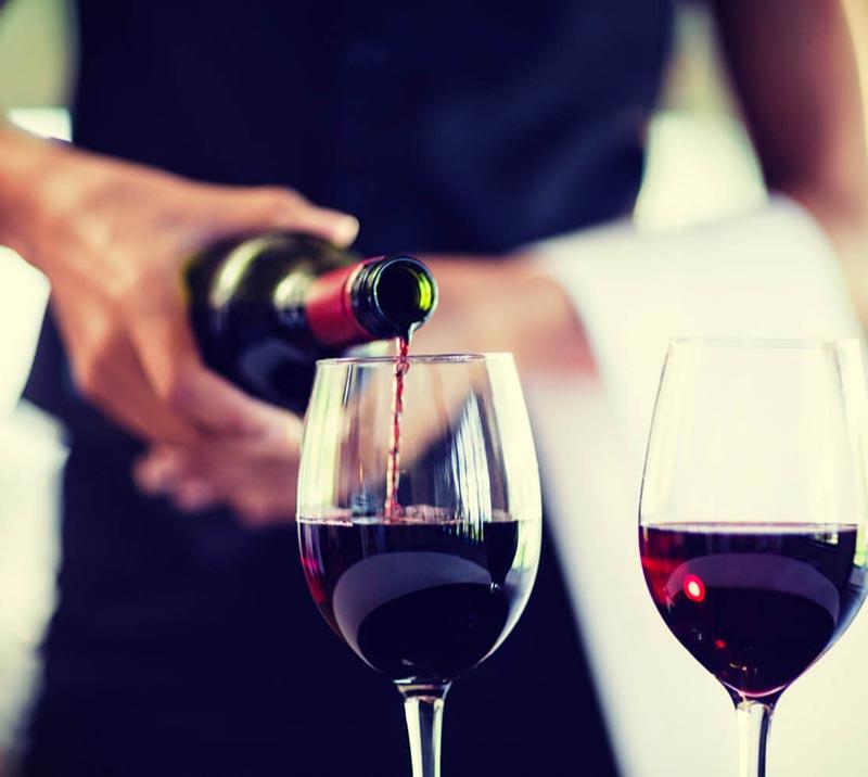 A member of waiting staff gently pours a glass of red wine