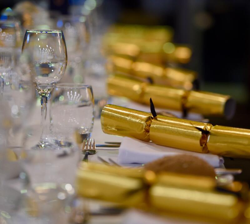 A festively laid table with a row of Christmas crackers and glasses